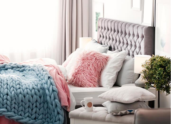 Cosy neutral coloured bedroom with velvet pink headboard, white bedding with chunky light blue wool knitted light throw